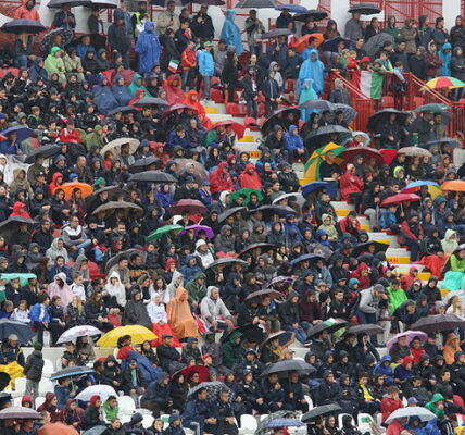 fans getting wet with umbrellas at football stadium without a roof