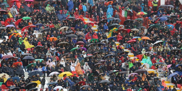 fans getting wet with umbrellas at football stadium without a roof