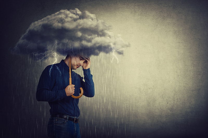 man standing under cloud in rain looking sad